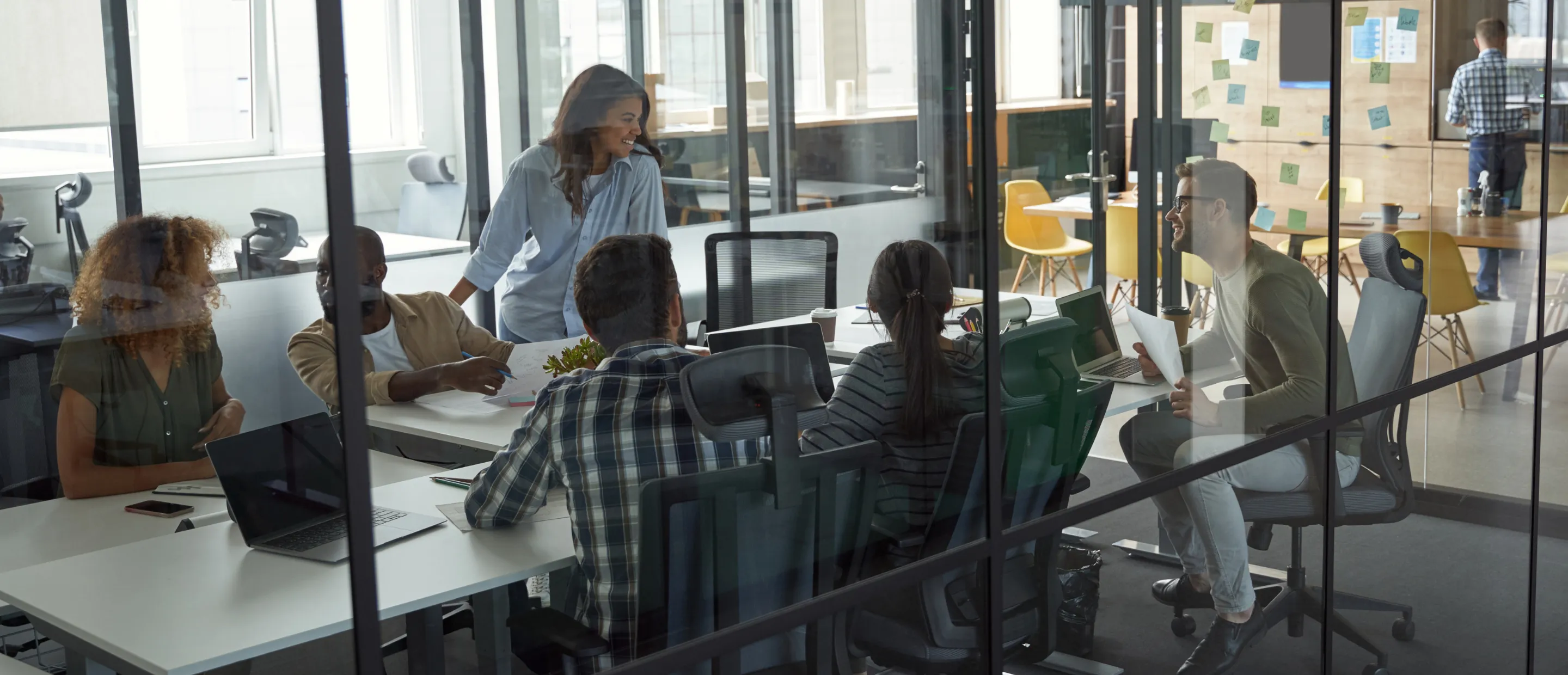 Group of people working on laptops around a table with a potted plant in the center.