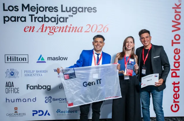 Three people in black enjoy IT shirts celebrating with confetti, one holding a certificate, under a congratulatory banner in an office.