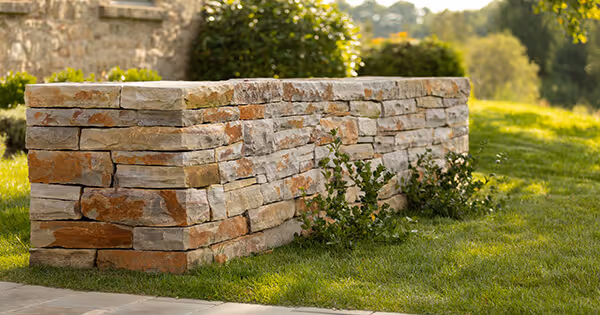 A decorative low stone wall surrounded by green grass and small plants in a sunny garden setting.