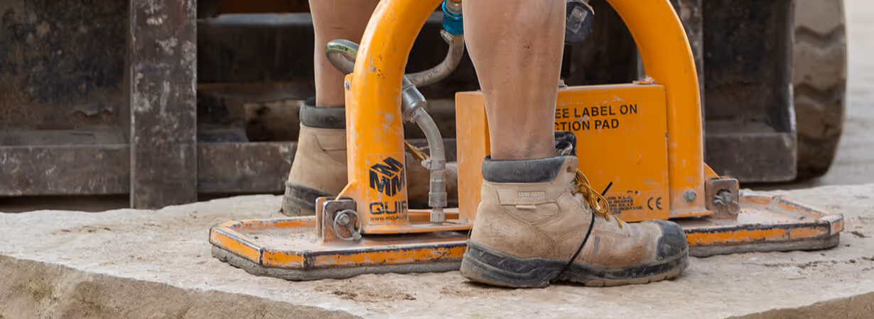 Close-up of a worker's dusty boots operating an orange compaction machine on a dirt surface.