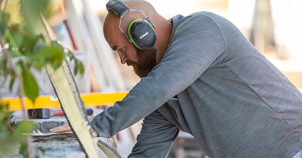 Low rectangular dry stone wall with green plants growing at its base on a grassy lawn.