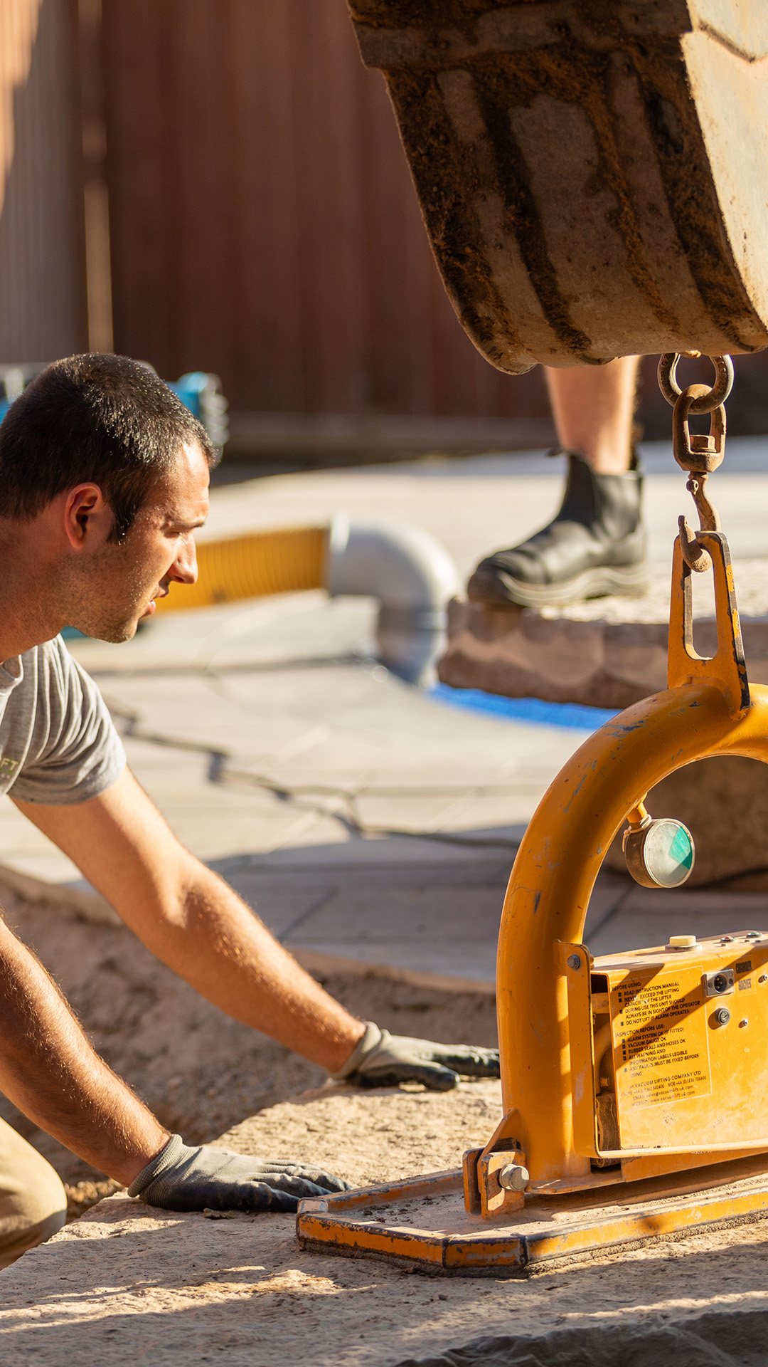 Bearded man wearing a grey Cedar Croft Landscape & Design jacket operating machinery with orange and black metal parts.