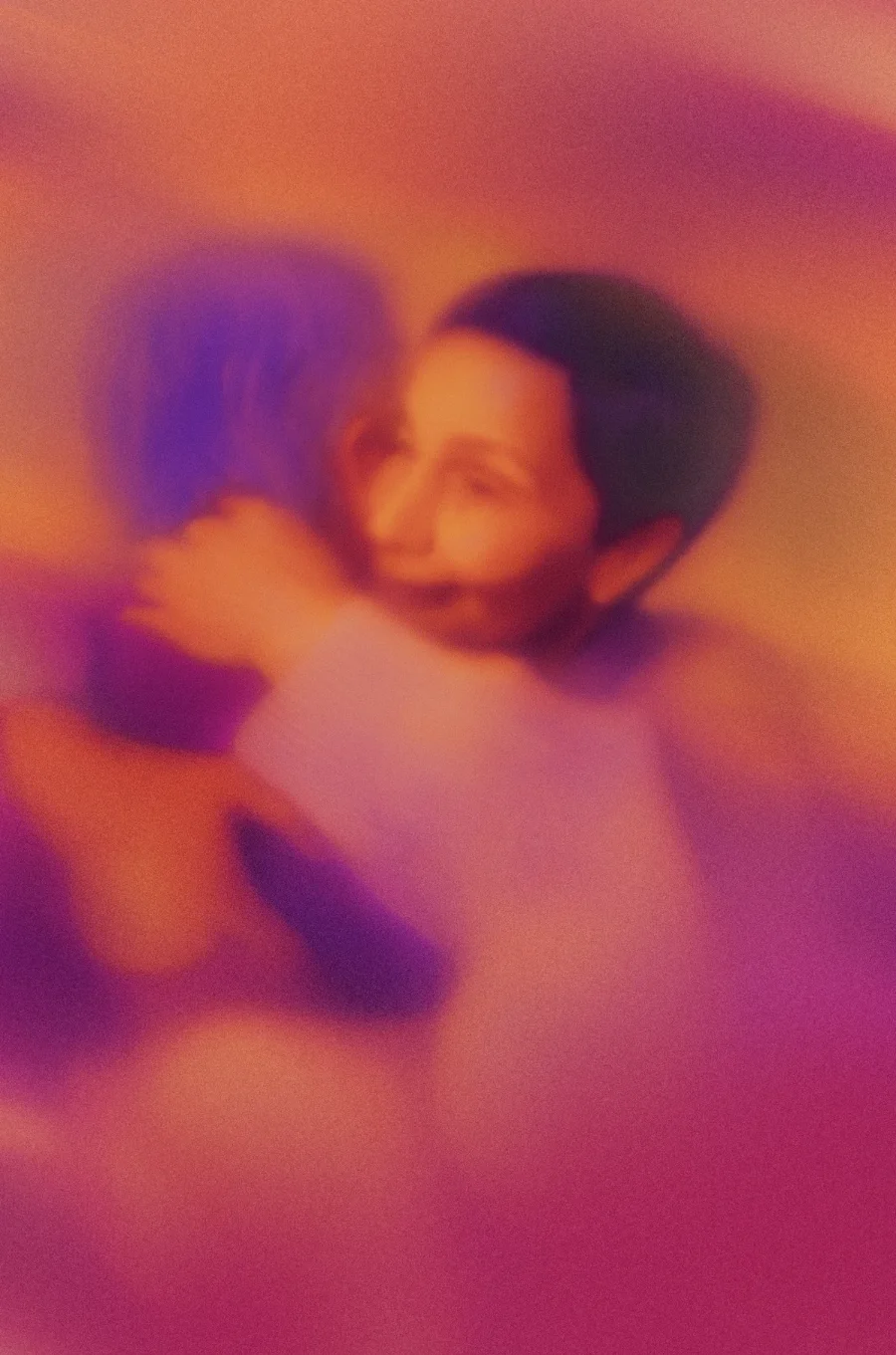 Soft-focus image of two people embracing warmly with a purple and orange color overlay.