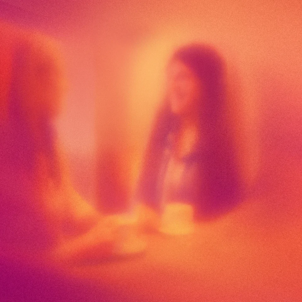 Blurred image of two people sitting and talking at a table with a cup.
