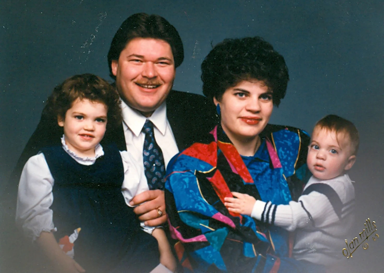 Family portrait of a man, woman, and two young children against a solid blue background.