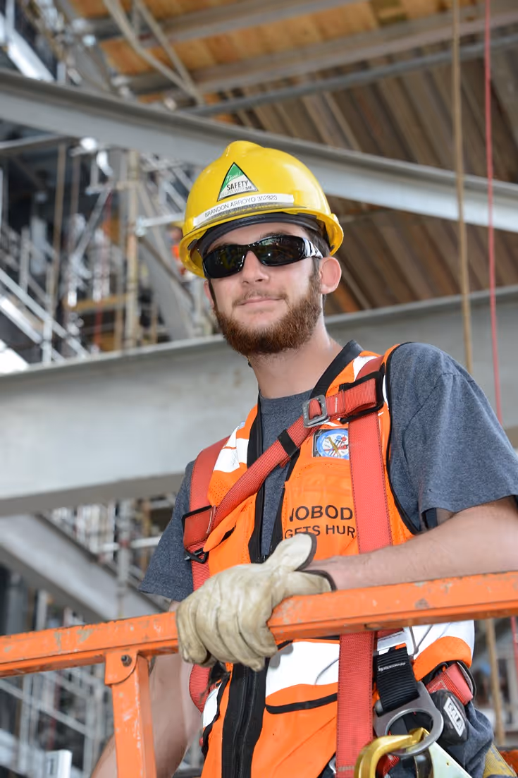 Construction worker wearing safety gear and a hard hat standing on scaffolding at a job site