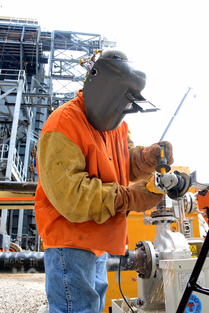 Pipefitter wearing protective gear welding a metal pipe at an industrial job site