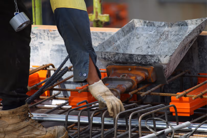 Worker securing metal rebar on a construction site with heavy equipment nearby
