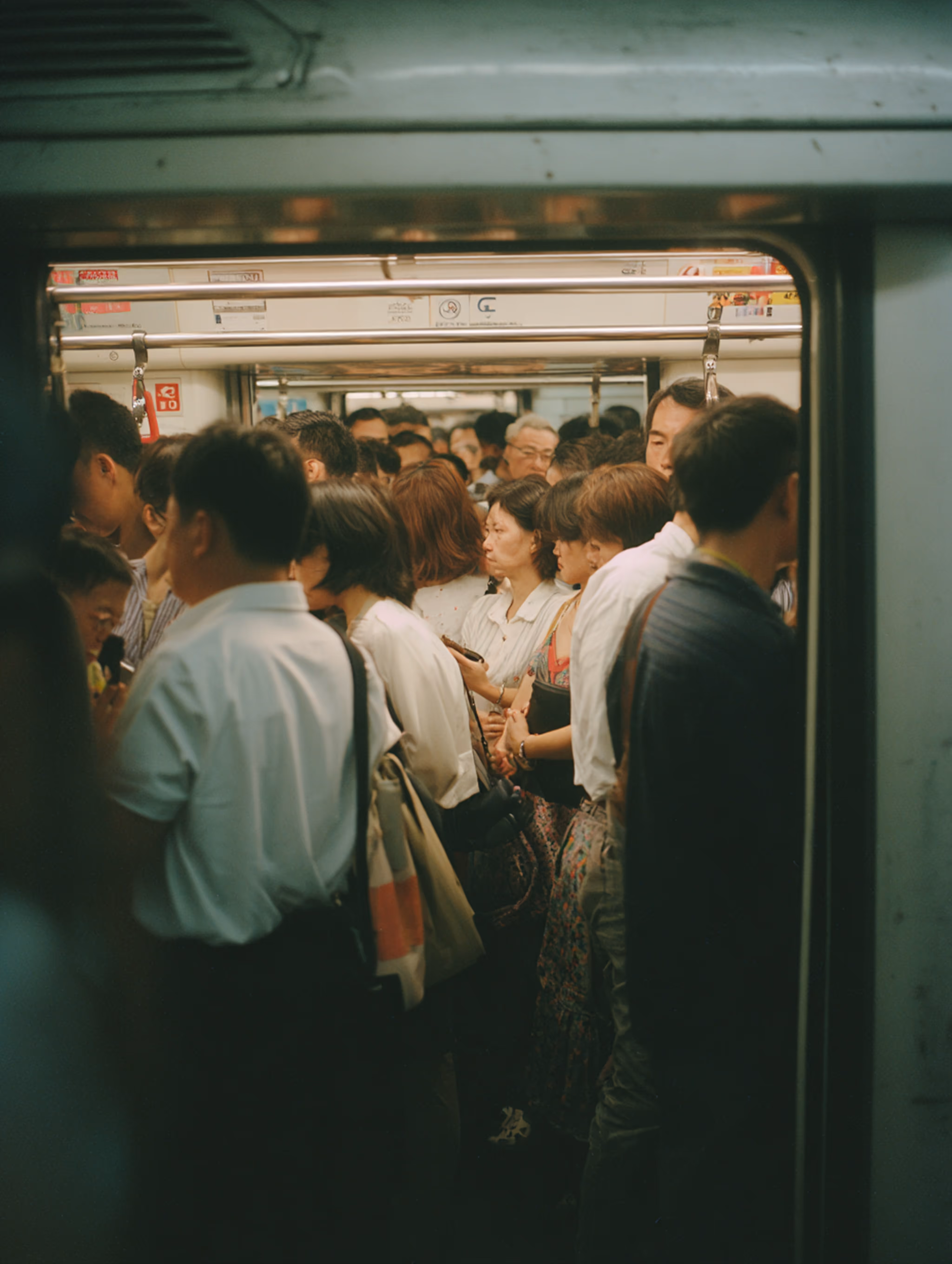 Crowded subway car filled with standing commuters, some holding onto overhead handrails.