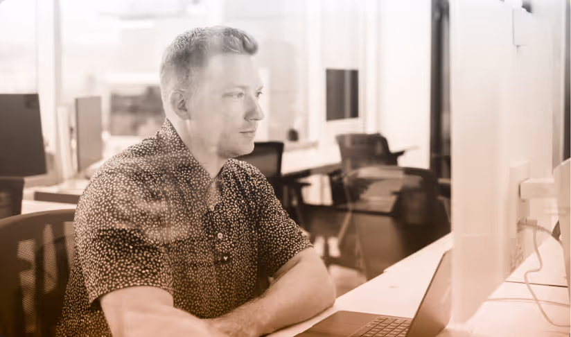 Man sitting at a desk, looking at a computer monitor in a modern office environment.