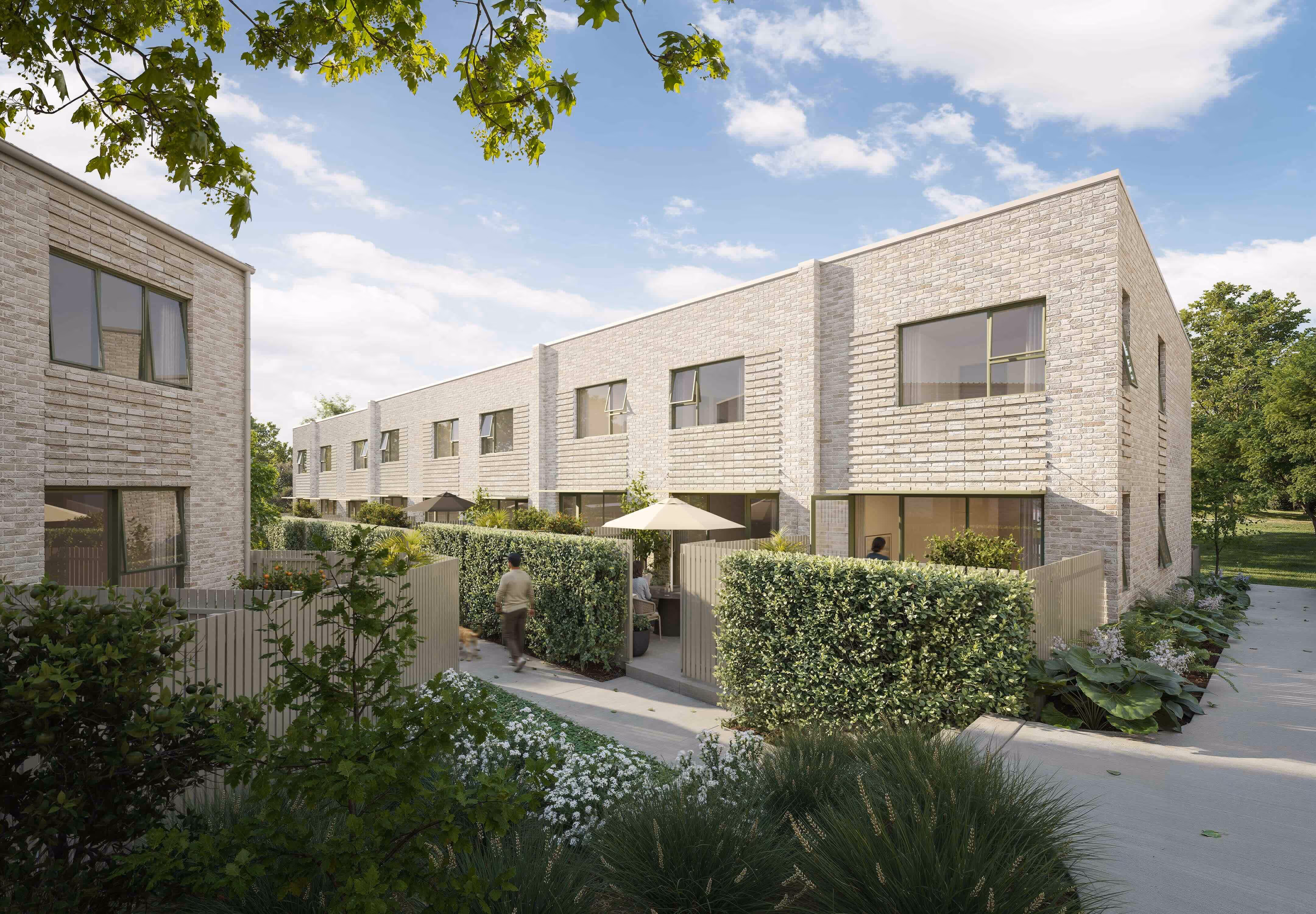 Modern two-story brick townhouses with private fenced garden patios and green shrubs under a partly cloudy sky.