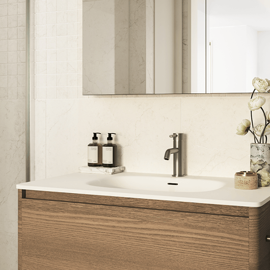 Modern bathroom sink with wood vanity, silver faucet, soap dispensers, and floral decor on a marble countertop.
