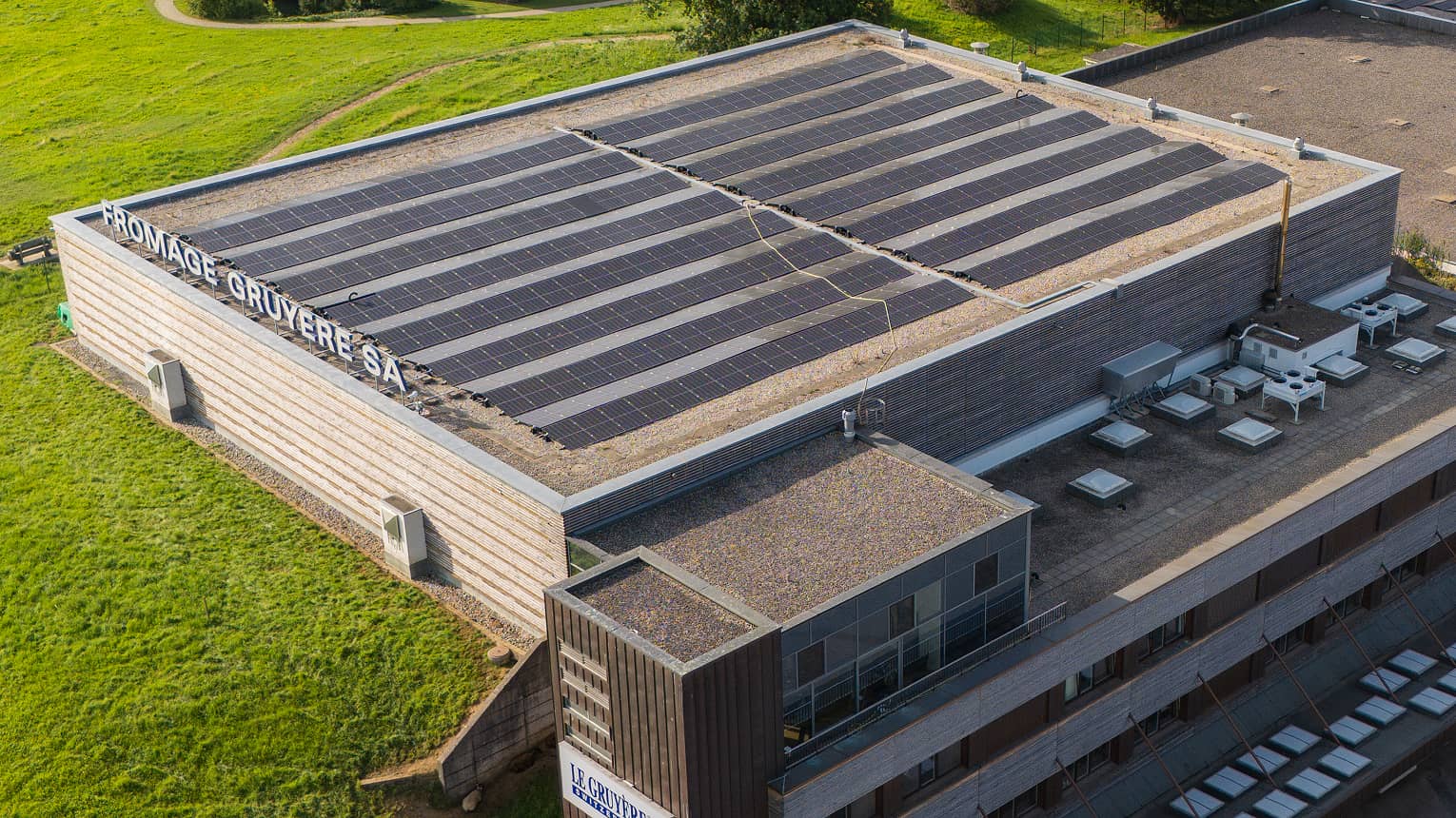 Vue aérienne d'un bâtiment à toit plat avec panneaux solaires et inscription « Fromage Gruyère SA » sur le côté.