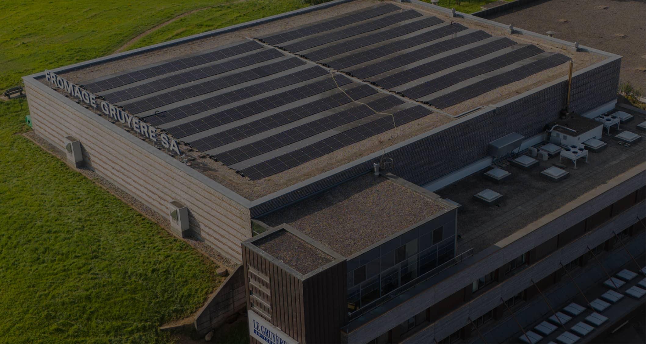 Bâtiment de l'entreprise Fromage Gruyère SA avec des panneaux solaires sur le toit plat entouré d'herbe verte.