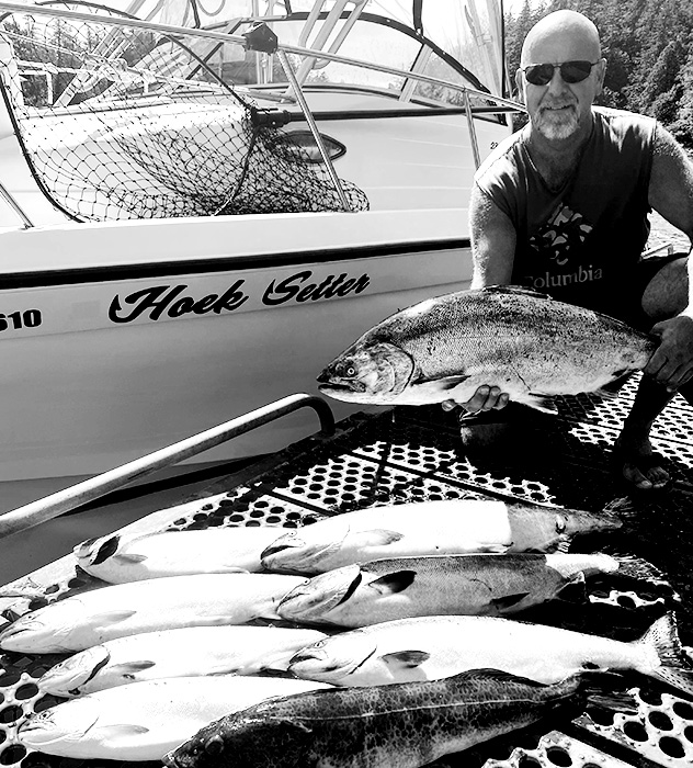 Person wearing sunglasses holding a large fish next to a boat labeled 'Hoek Setter' with several other fish laid out on the dock.
