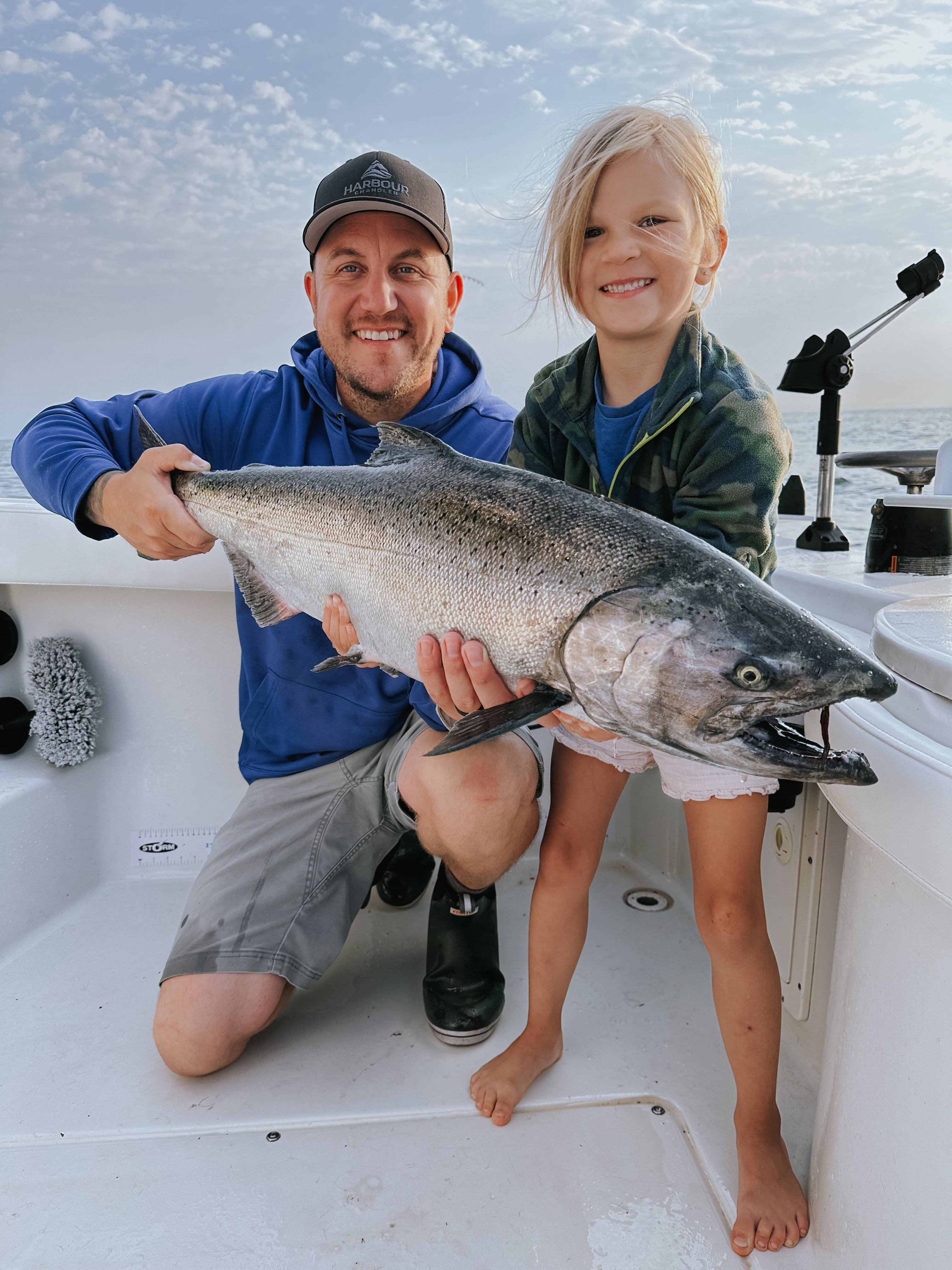 Man and young girl smiling on a boat holding a large fish they caught.