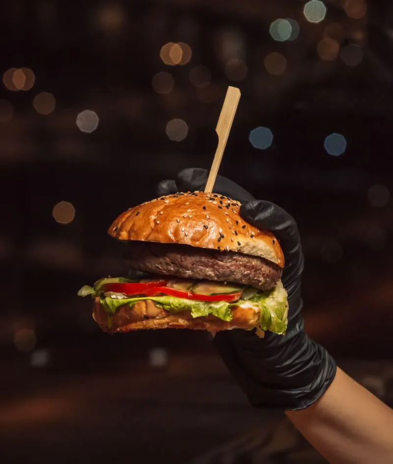 A hand holding a hamburger with a toothpick in it.