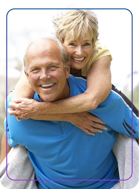 Smiling elderly woman giving a piggyback ride to an elderly man outdoors.