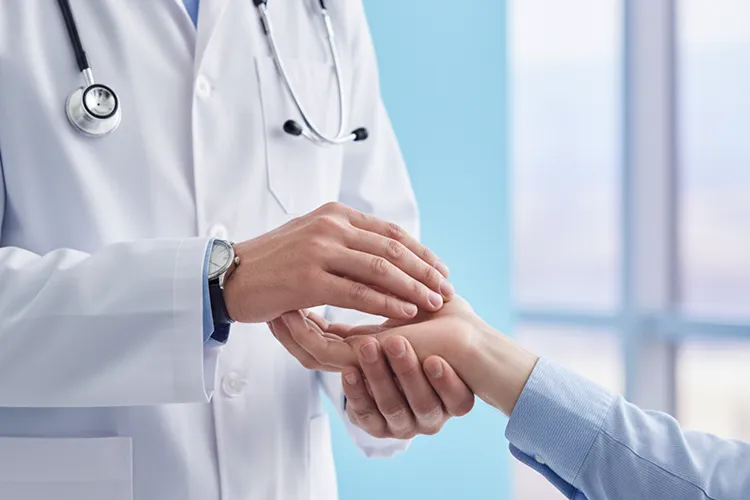 Doctor in white coat and stethoscope examining a patient's wrist in a bright medical office.
