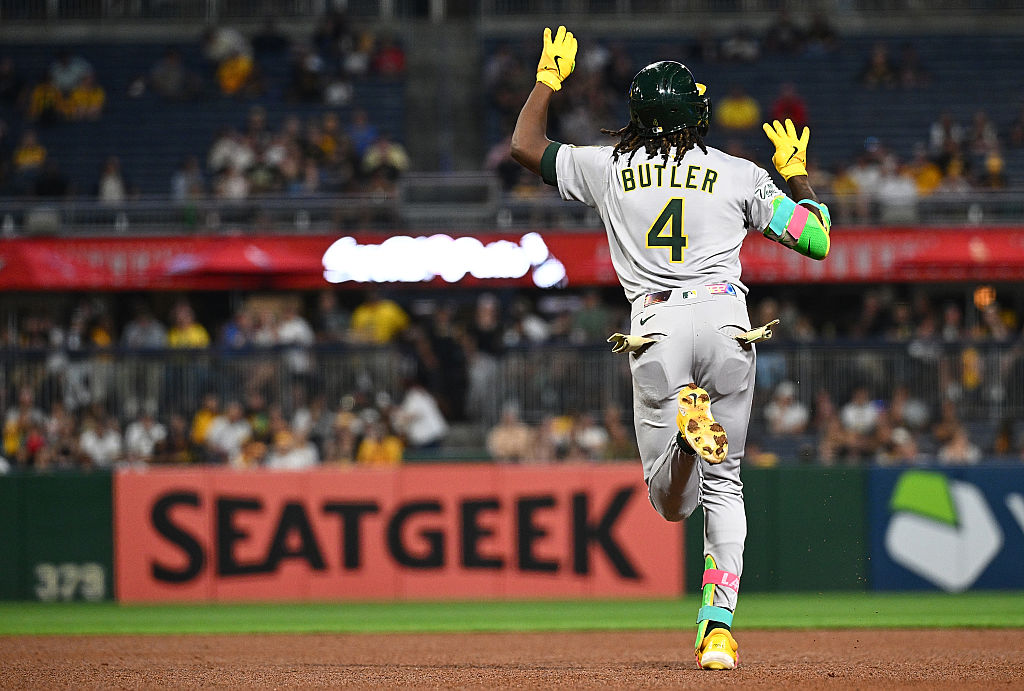 A baseball player wearing number 4, labeled Butler, runs the bases with arms raised during a game, with fans blurred in the background.