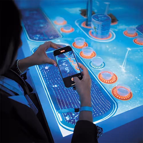 Person using smartphone to take photo of illuminated interactive game table with colorful chips and digital display.