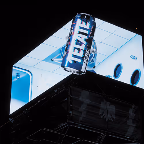 Large digital screen displaying a can of Tecate Light beer against a blue and white geometric background at night.
