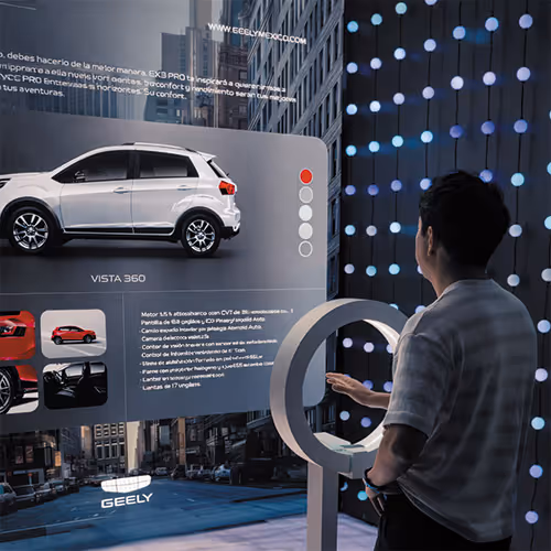 Person interacting with a digital display showcasing a 360-degree view and features of a white Geely car in a modern showroom environment.