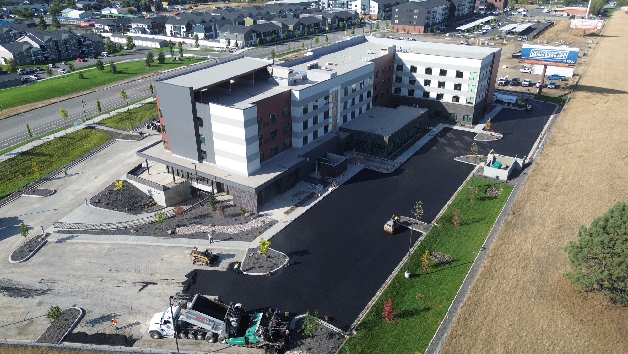 Aerial view of a multi-story building under construction with workers paving the parking lot.