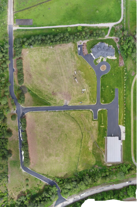 Aerial view of a house with a circular driveway, open fields, and paved roads surrounding it.