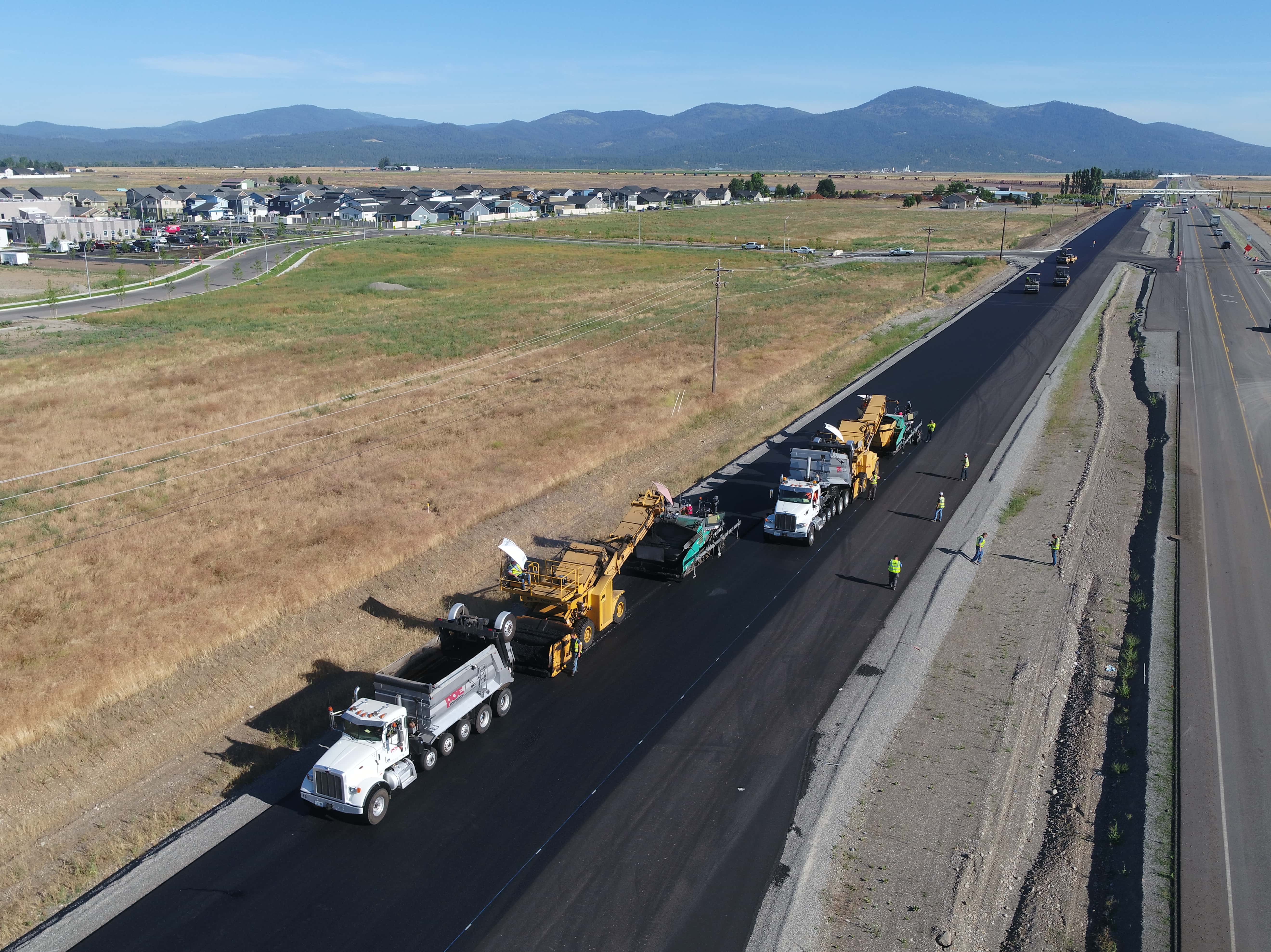 Aerial view of road construction with paving trucks and workers laying asphalt on a highway.