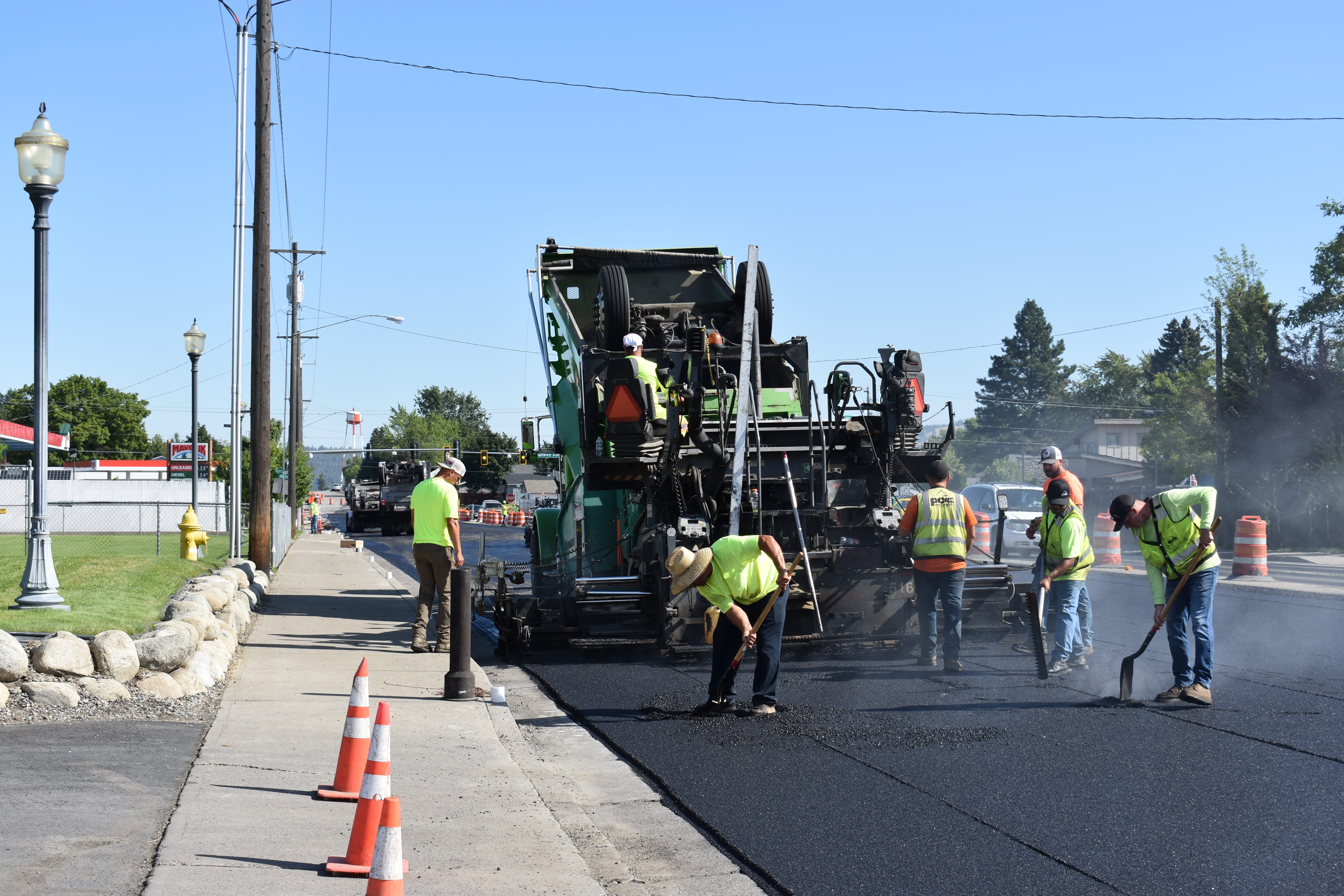 Construction workers paving a road with heavy machinery on a clear, sunny day.