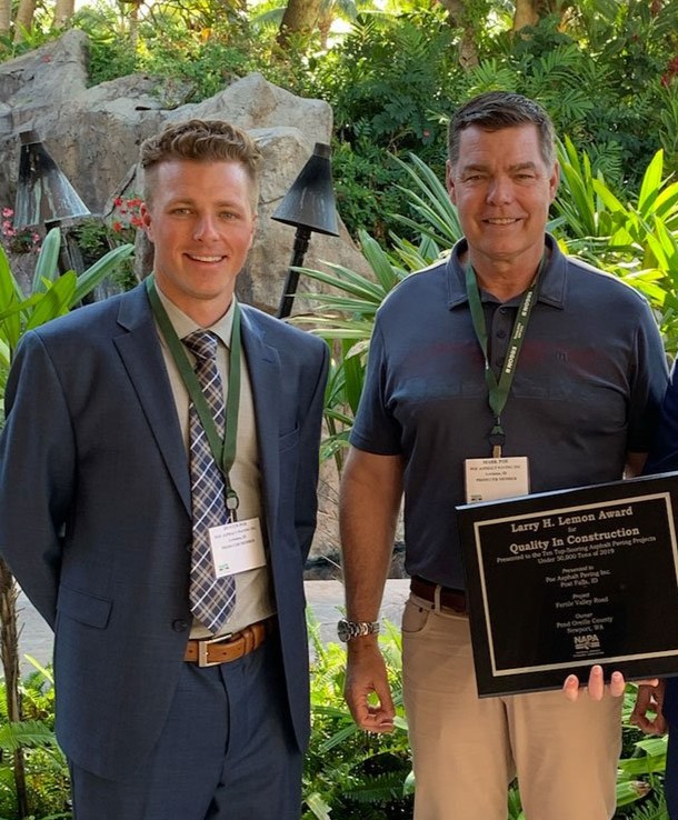 Two men with name badges, one holding a Larry H. Lemon Award plaque, standing outdoors near plants.