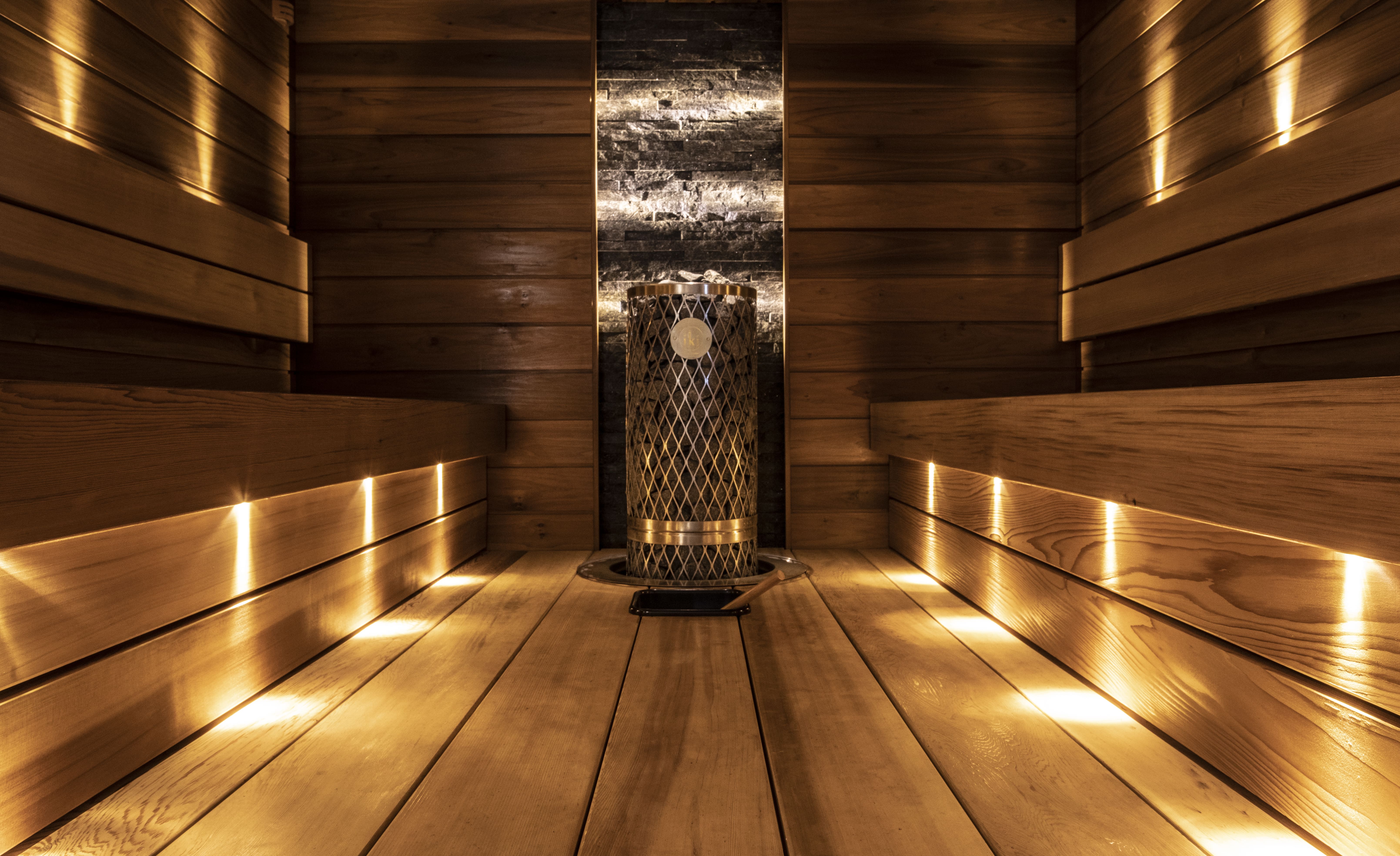 Puinen sauna, jossa on penkit molemmin puolin ja keskellä kiuas kivetäytteisellä säiliöllä.