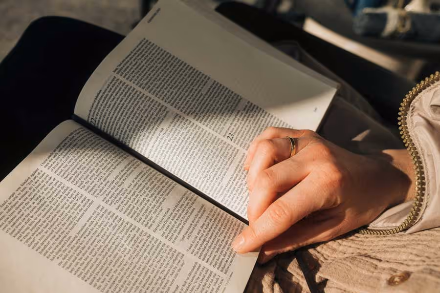 A closeup shot of a female reading a Bible while using her finger to follow the lines.