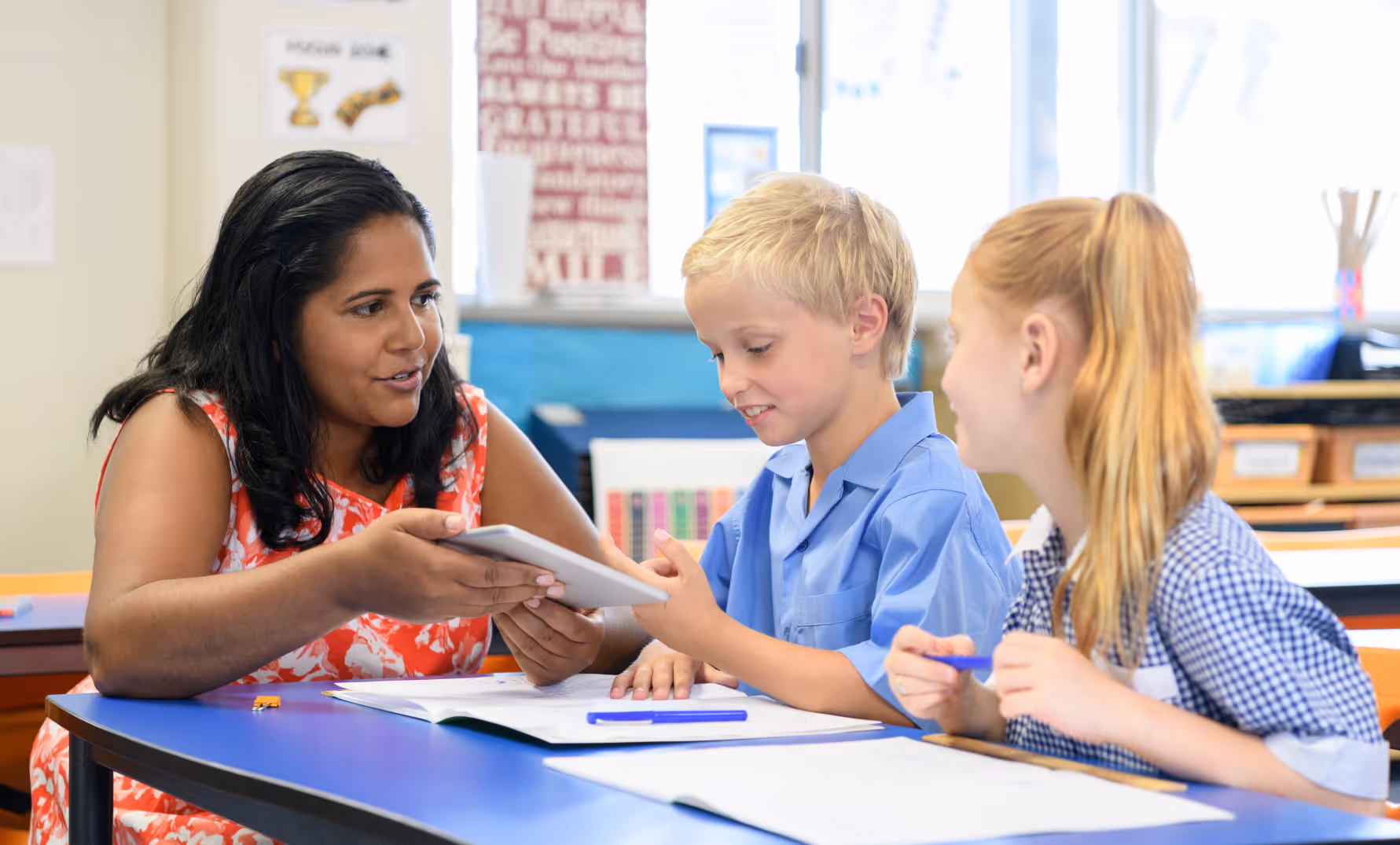 Teacher assisting primary school student using a tablet for classroom assessment activity.