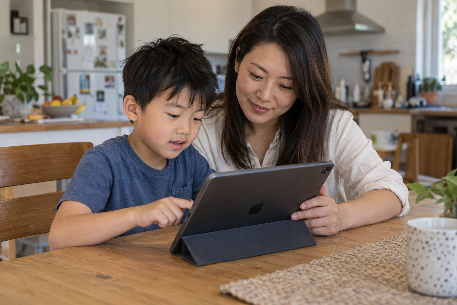 A mother and her young son look at a tablet together at the kitchen table as he practises.