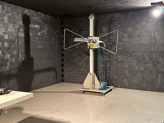 Testing device with two large wire antennas in a room with dark, perforated walls and ceiling.