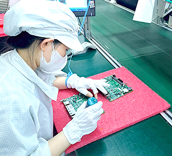 Factory worker in white uniform assembling or inspecting electronic components at workstation.