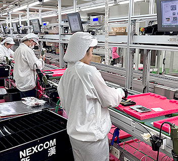 Factory workers in white gowns assembling electronics on a conveyor belt at Nexcom.