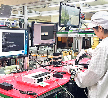 Technician in cleanroom attire working at a workstation with multiple monitors and electronic equipment.