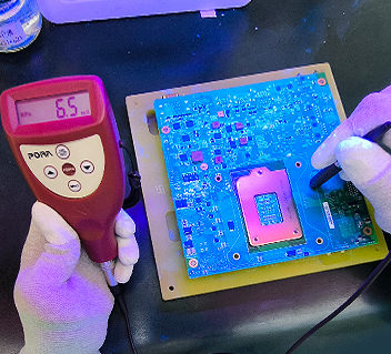 Hands holding a coating thickness gauge and probe measuring an electronic circuit board.