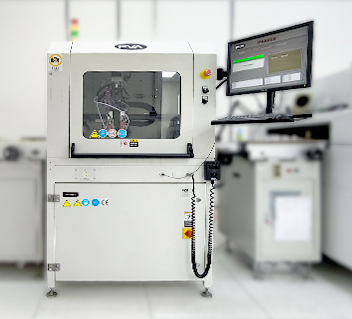 White industrial machine with windowed compartment and attached computer monitor on a desk in a lab.