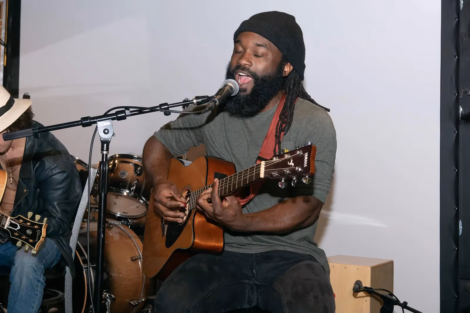 George performing seated with a guitar and microphone in a warm indoor setting.