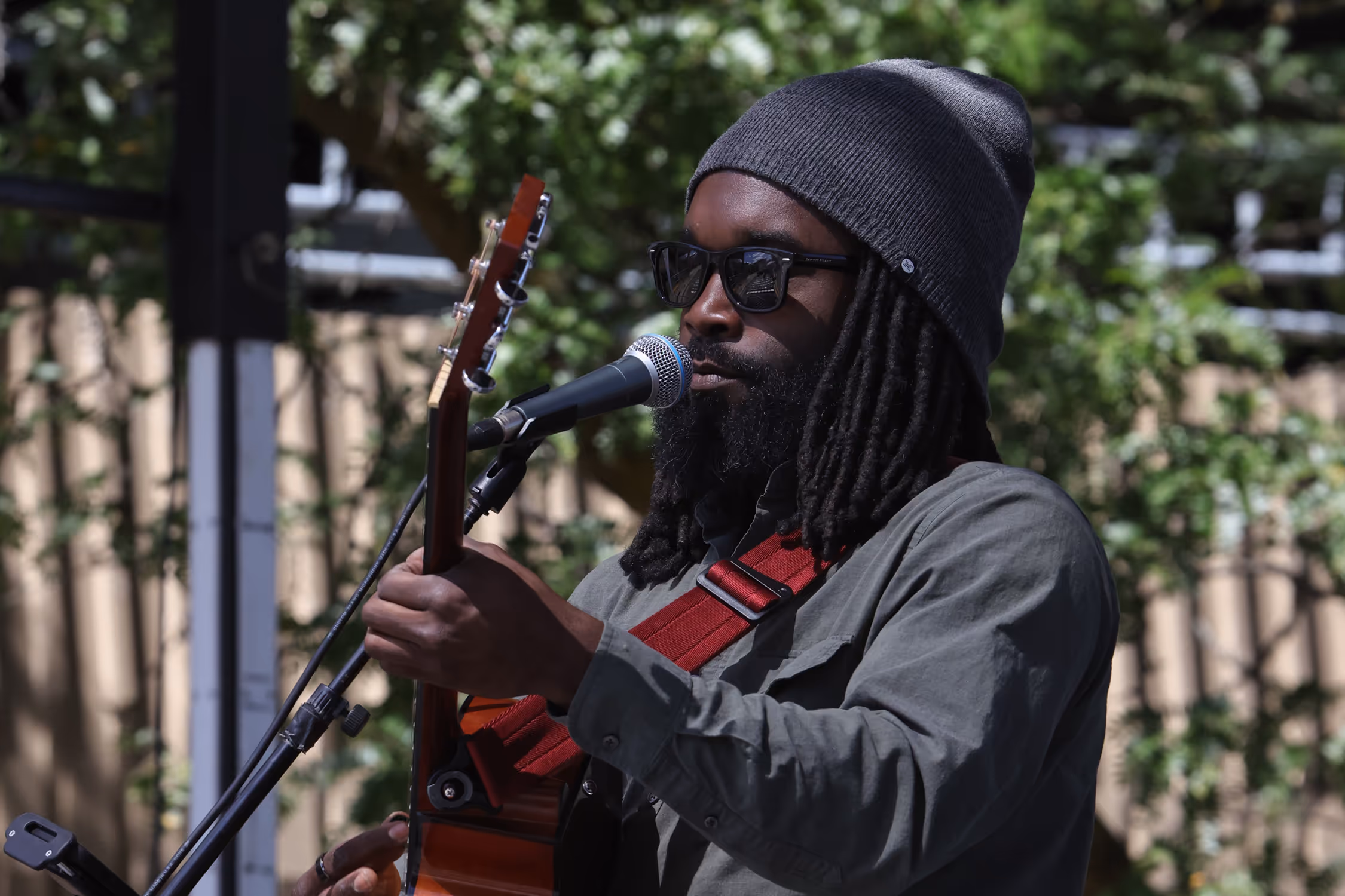 George singing outdoors while playing guitar, surrounded by trees.