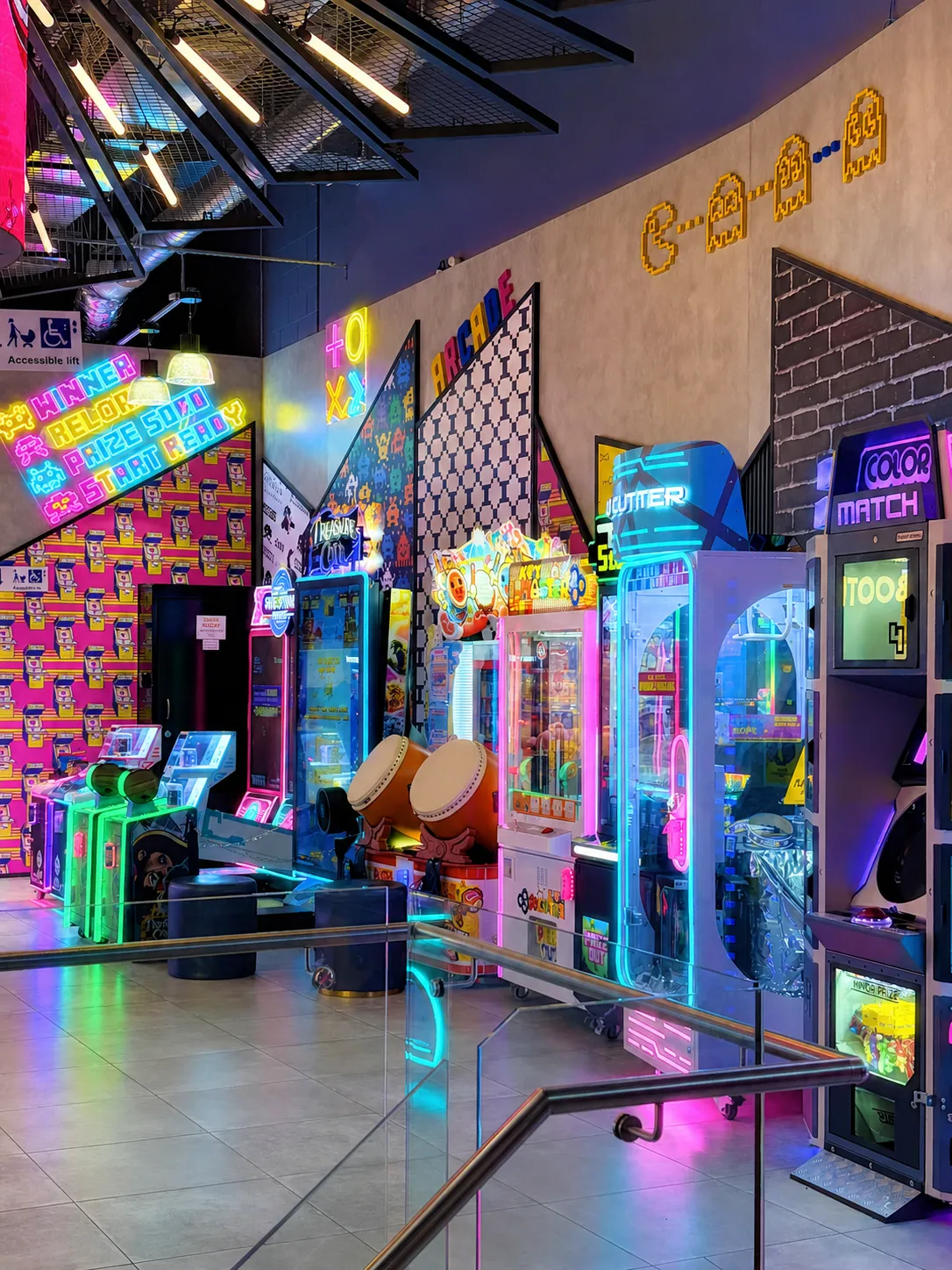 Neon-lit arcade walkway with claw machines and drum games at KOKO Amusement