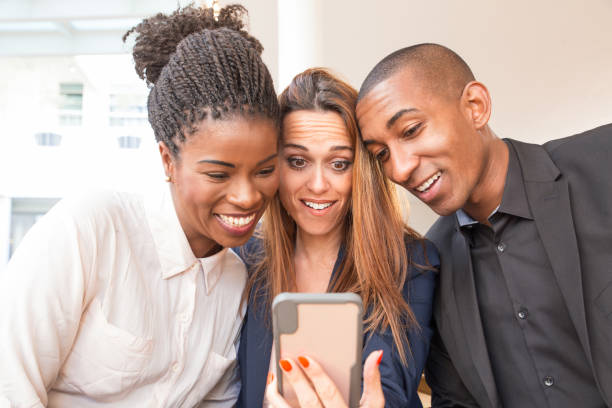 three smiling colleagues looking at a phone in amazement