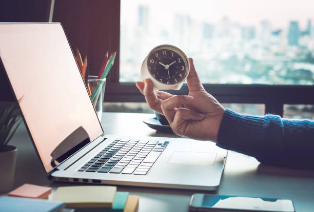 businessman holding clock while looking at laptop