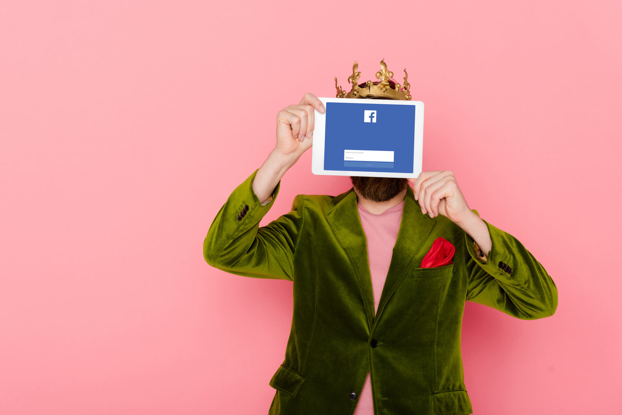 man with crown hiding his face behind a tablet showing facebook