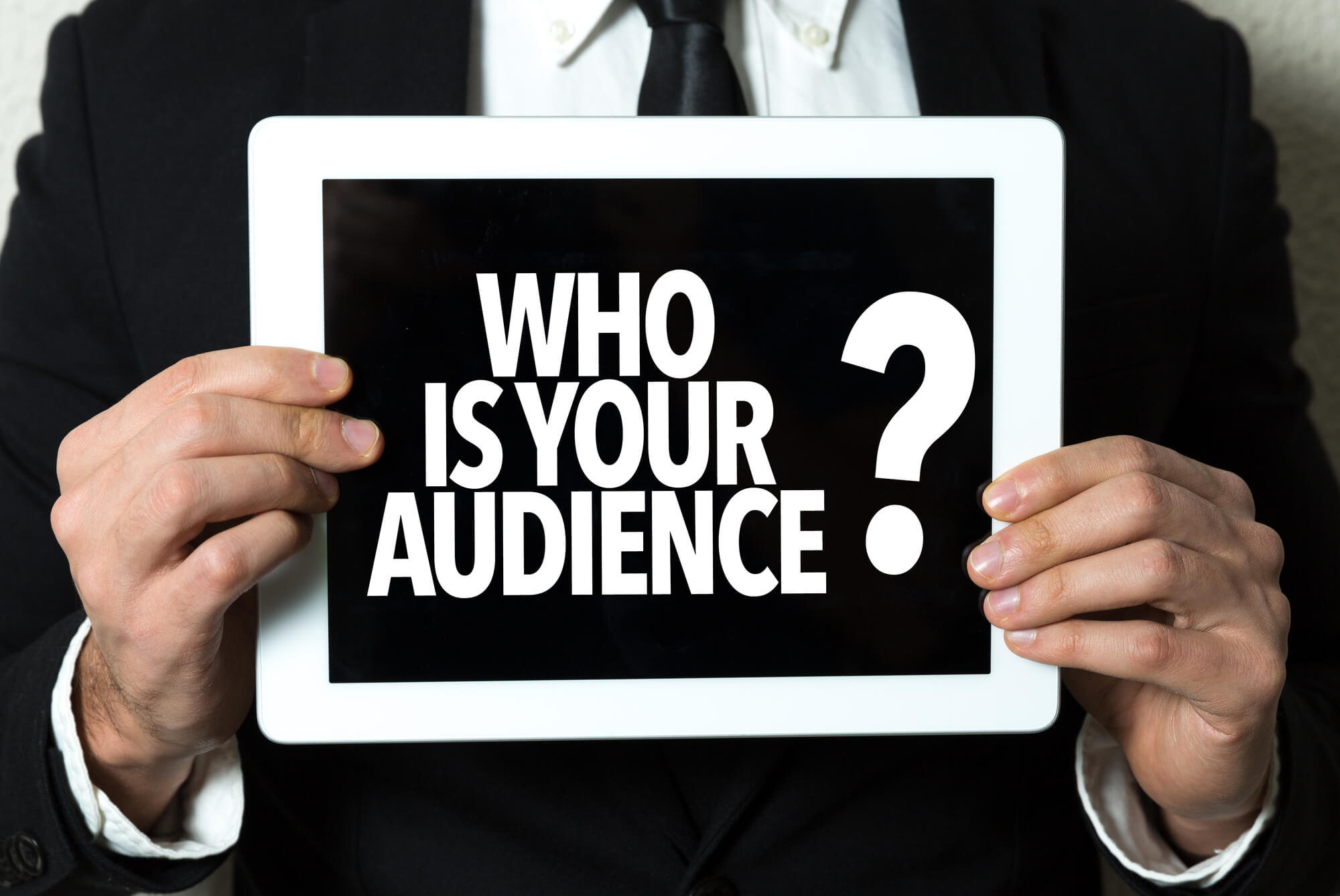 businessman holding tablet with "who is your audience" on screen