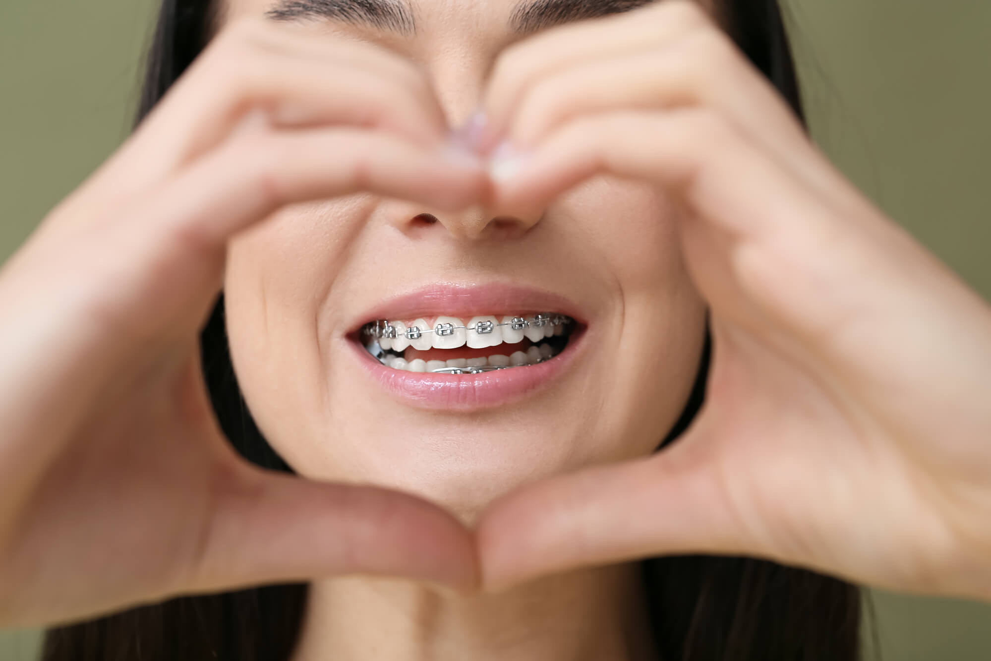 happy woman posing with heart sign focusing on her braces